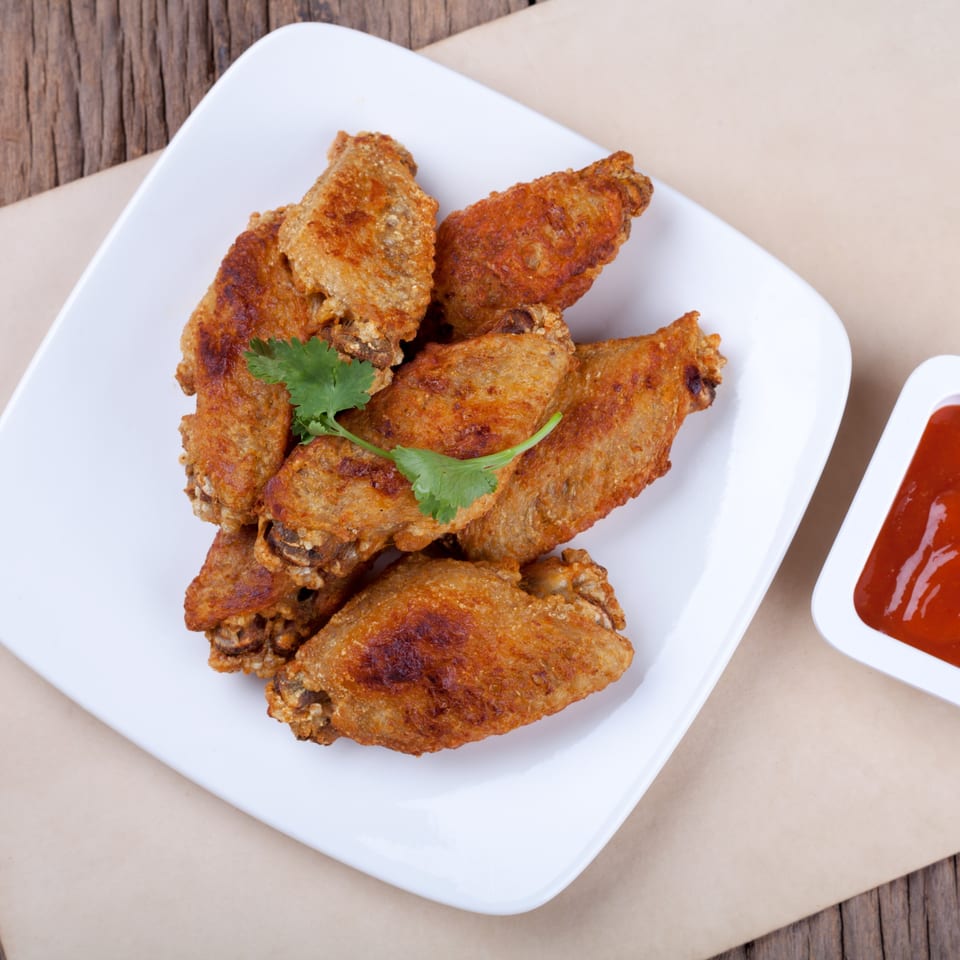 Crispy fried chicken wings with a sprig of cilantro on a white plate, with a side of red sauce.