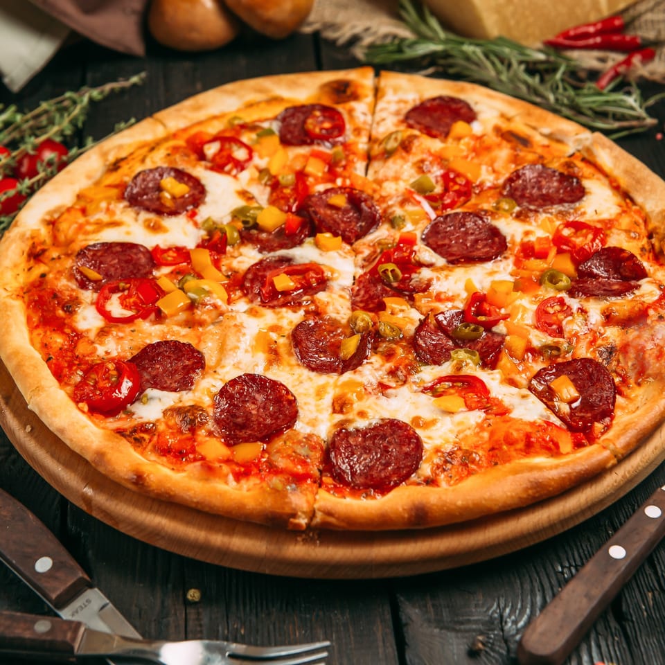 Pepperoni pizza with colorful bell peppers and melted cheese on a wooden board.