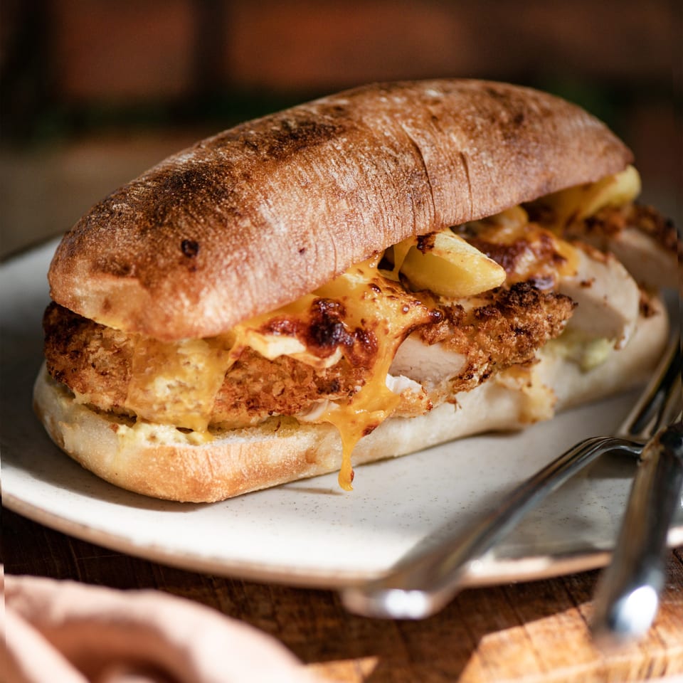 A toasted sub sandwich with crispy chicken, melted cheese, and fries on a white plate.
