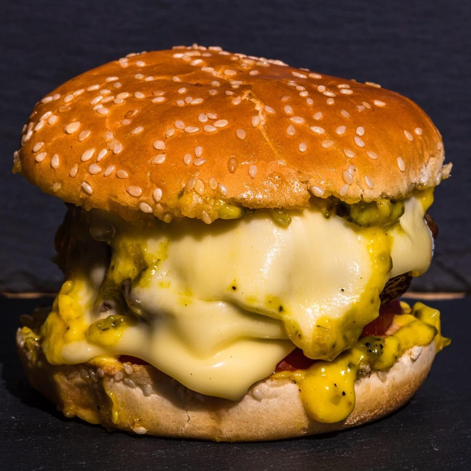 A large, juicy burger with melted cheese and a sesame seed bun on a dark surface.