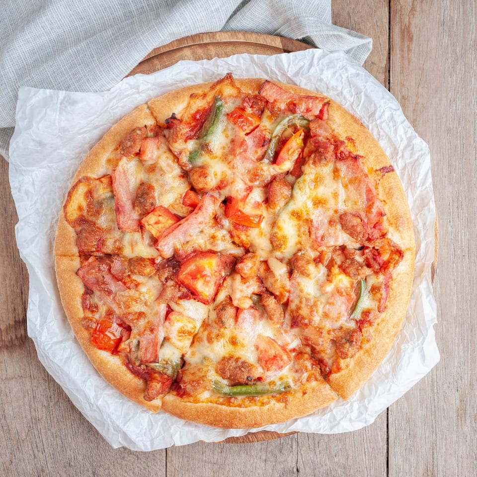 A Northwood House of Pizza & Subs pizza with melted cheese, ham, and vegetables on a wooden table.