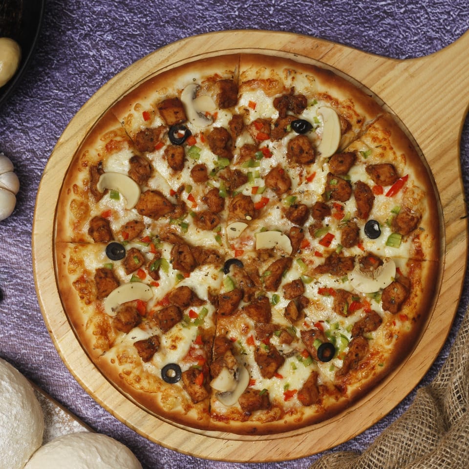 A Northwood House of Pizza & Subs pizza with chicken, mushrooms, olives, and peppers on a wooden board.